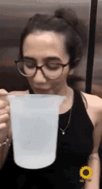 a woman wearing glasses is drinking from a plastic pitcher .