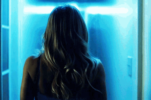 a woman with long hair is standing in a doorway with a blue light behind her