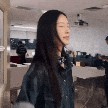 a woman with long black hair is standing in an office