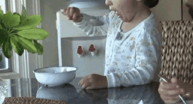 a little girl is sitting at a table with a spoon in her hand