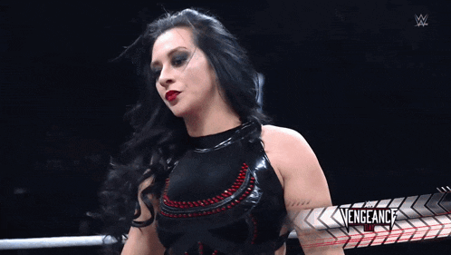a woman in a black dress is standing in a ring with a sign that says the vengeance on it