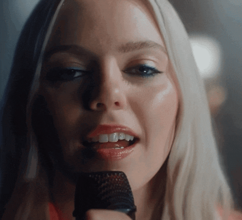 a blonde woman singing into a microphone with her mouth open