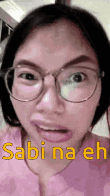 a woman wearing glasses and a pink shirt says sabi na eh in yellow letters