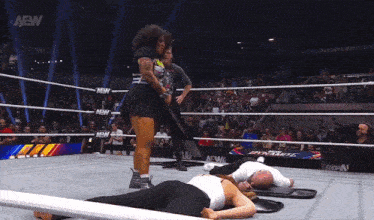 a woman in a black skirt is standing next to a man laying on the ground in a wrestling ring