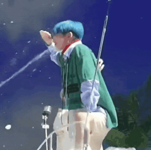 a man with blue hair is standing in front of a microphone and spraying water on himself .