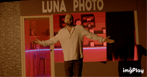 a man stands in front of a luna photo store with his arms outstretched