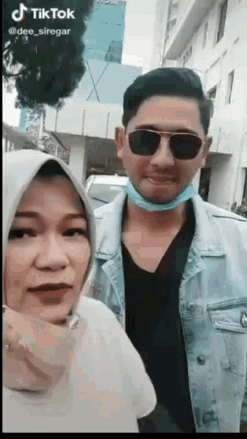 a man and a woman are posing for a picture while wearing sunglasses and a mask .