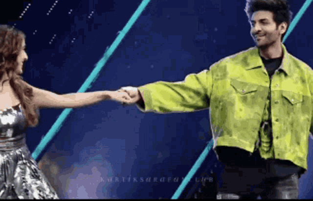 a man in a green jacket and a woman in a silver dress are holding hands on a stage .