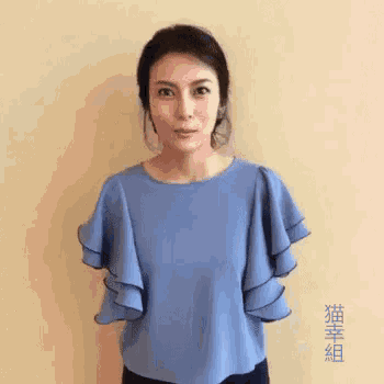 a woman in a blue top with ruffled sleeves is standing in front of a beige wall .