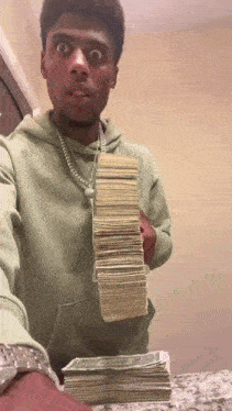 a man in a green hoodie is holding a stack of money ..