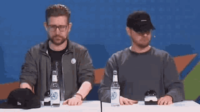 two men are sitting at a table with bottles of water on it .