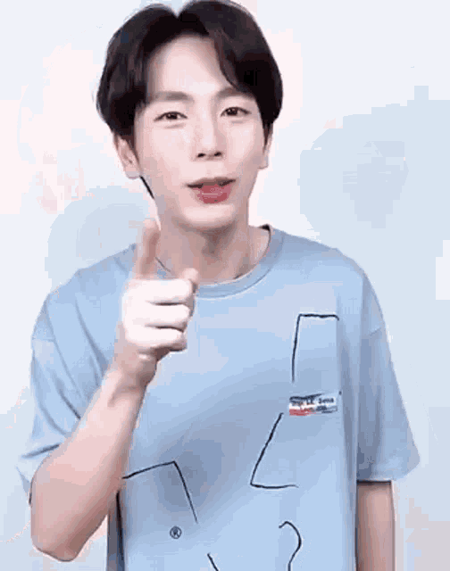 a young man is wearing a blue t-shirt and giving a thumbs up .