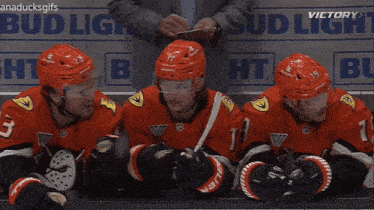 a group of hockey players are sitting on a bench in front of a bud light advertisement