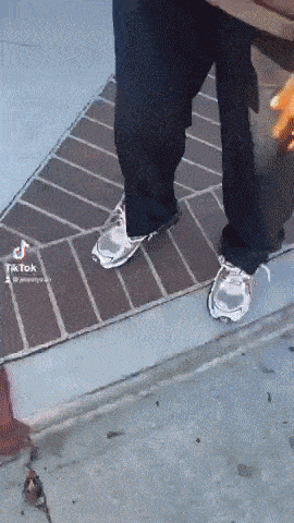 a person is standing on a sidewalk wearing a pair of silver sneakers
