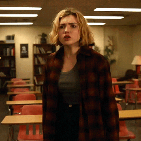 a woman in a plaid shirt stands in a classroom with red chairs