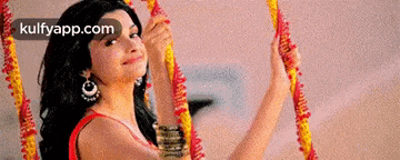 a woman in a red dress is holding a yellow and red flower garland .