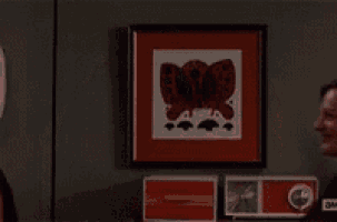 a man and a woman are clapping in front of a framed picture with a butterfly on it