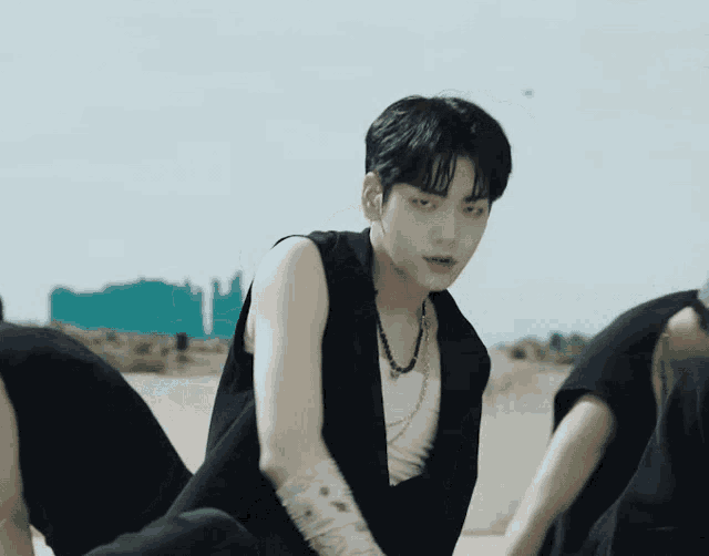 a young man in a black vest and a white tank top is dancing in a group .