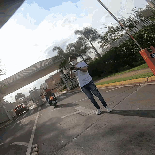a man wearing a mask takes a picture of a man on a scooter