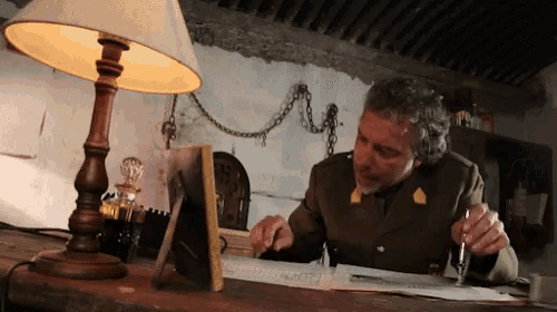 a man sits at a desk with a lamp and a picture frame