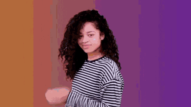 a woman with curly hair wearing a striped shirt is dancing on a purple background .