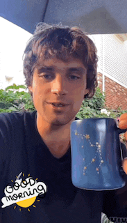 a man wearing a black shirt that says good morning holds a blue mug
