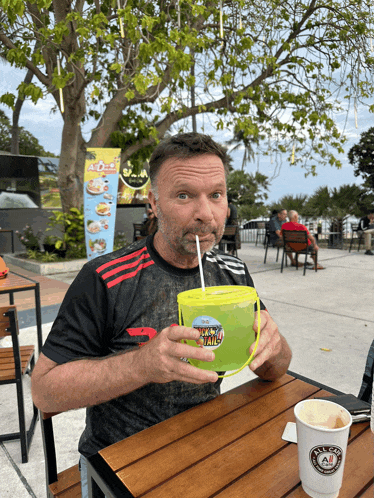 a man sitting at a table drinking from a yellow cup that says ' thailand ' on the front