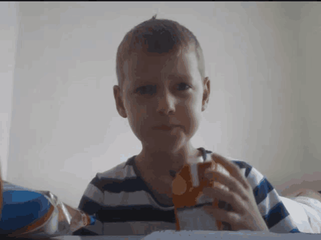 a young boy in a striped shirt is drinking orange juice from a bottle