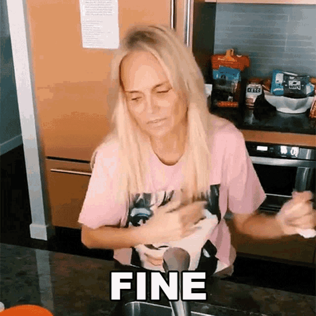 a woman in a pink shirt is washing dishes and the word fine is on the counter in front of her