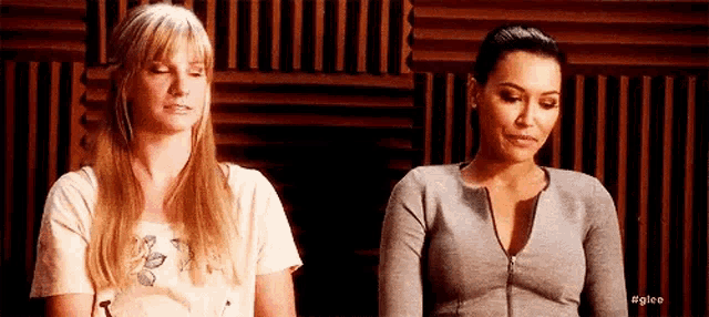 two women are sitting next to each other in a room with a wooden wall .