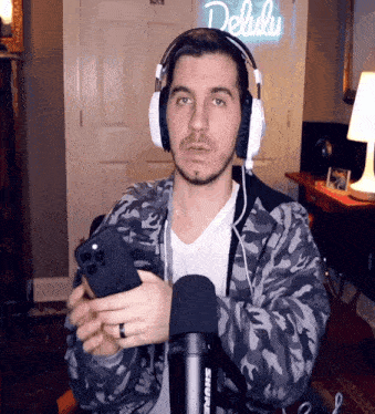 a man wearing headphones is holding a cell phone in front of a neon sign that says delulu