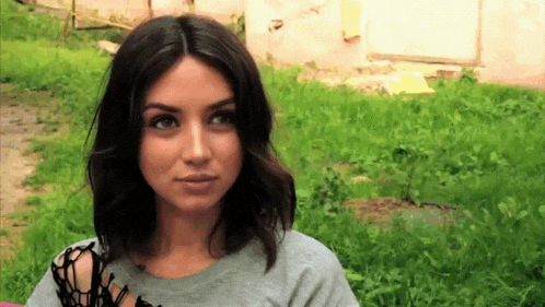 a woman wearing a gray shirt is standing in the grass