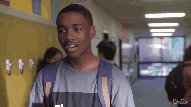 a young man with a backpack stands in a hallway with brat tv written on the bottom