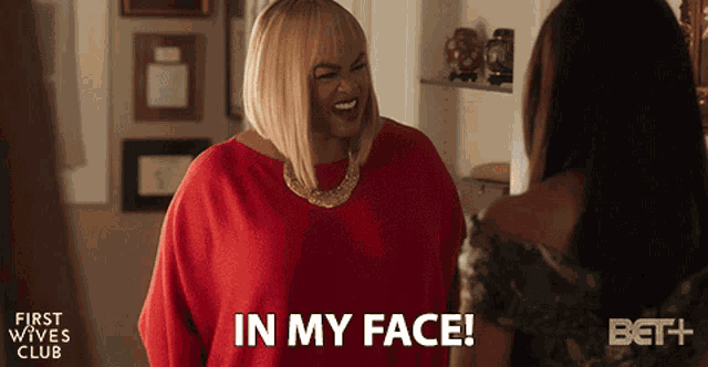 a woman in a red shirt says " in my face " while laughing