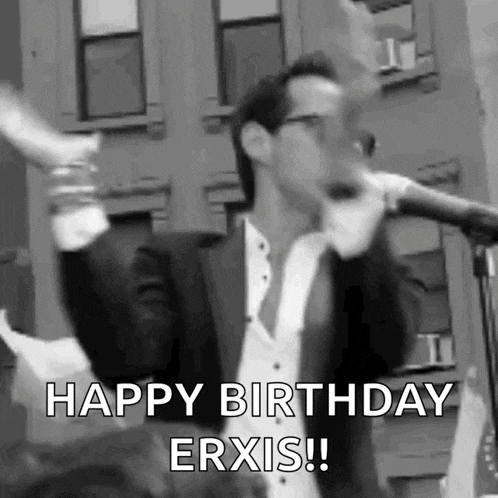 a man in a suit and tie is singing into a microphone and says `` happy birthday erxis '' .