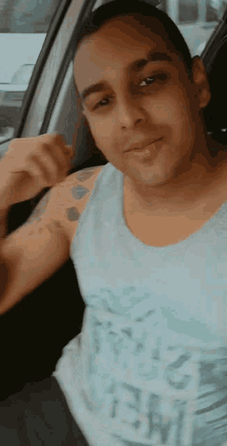 a man in a tank top with the word new on it is sitting in the driver 's seat of a car