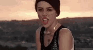 a woman wearing a beanie and a black tank top is standing on top of a hill .