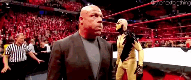 a man in a suit is standing in a wrestling ring next to a man in a gold costume .