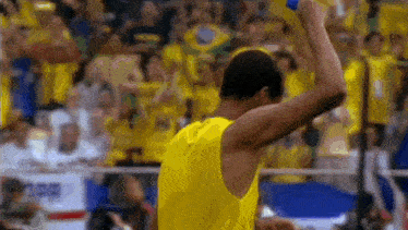 a man in a yellow tank top is standing in front of a crowd holding a blue object .