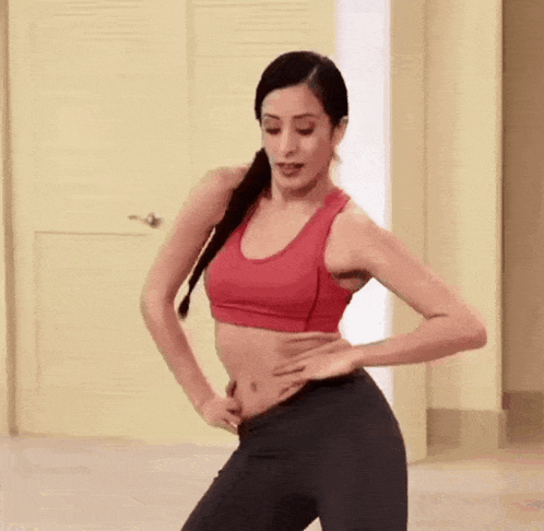 a woman in a red sports bra is dancing in a room .