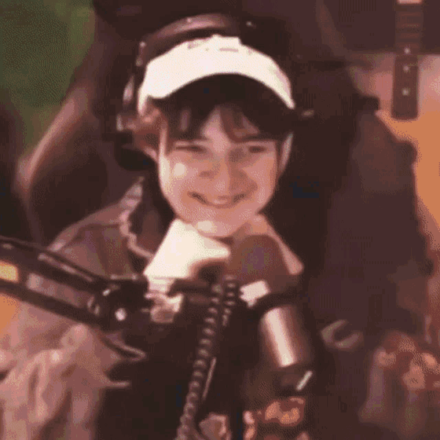 a young boy is sitting in front of a microphone wearing headphones and a hat .