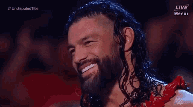roman reigns is smiling while standing in front of a crowd on a wrestling show .