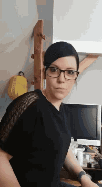 a woman wearing glasses and a black shirt is standing in front of a computer .