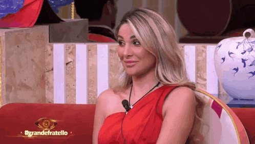 a woman in a red dress is sitting on a couch with a sign that says grandefratello