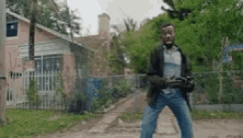a man is standing on a dirt road holding a remote control in front of a house .
