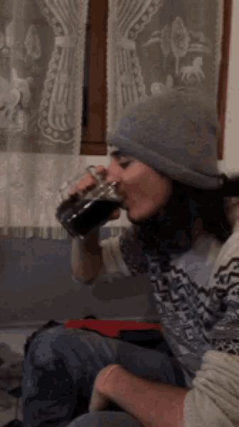 a man wearing a beanie is drinking from a mug