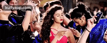 a woman in a red dress is dancing in a crowd of people while a man takes a picture of her .