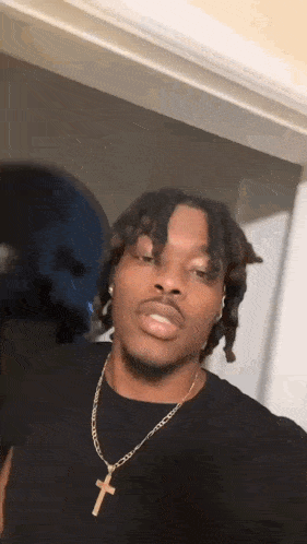 a young man wearing a black shirt and a gold chain with a cross pendant .