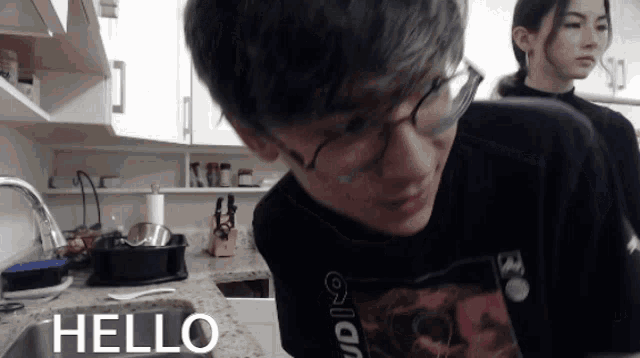 a man wearing glasses stands in front of a kitchen sink with the words hello written on it