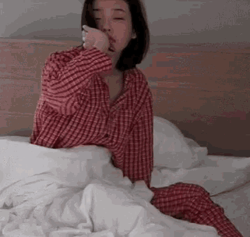 a woman in a red and white plaid shirt is sitting on a bed